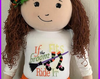 May include: A plush doll with brown yarn hair, a black and orange hair bow, and a white long-sleeve shirt. The shirt features the embroidered text If the broom Fits Ride It, a black broomstick, and two striped witch legs with black shoes.