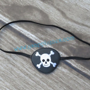 Könnte beinhalten: Ein schwarzes Augenpflaster mit einem weißen Totenkopf- und Knochenkreuz-Design. Das Augenpflaster hat ein elastisches Band.