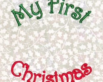 May include: A fabric featuring a light-colored background with a subtle, repeating white and light gray holly leaf pattern. The text "My First" is embroidered in green thread at the top, and the word "Christmas" is in red thread below it.