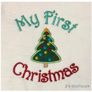 May include: An embroidered design on white fabric featuring a green Christmas tree with colorful ornaments and a yellow star topper. The text "My First" is stitched in teal above the tree, and "Christmas" is stitched in red below the tree.