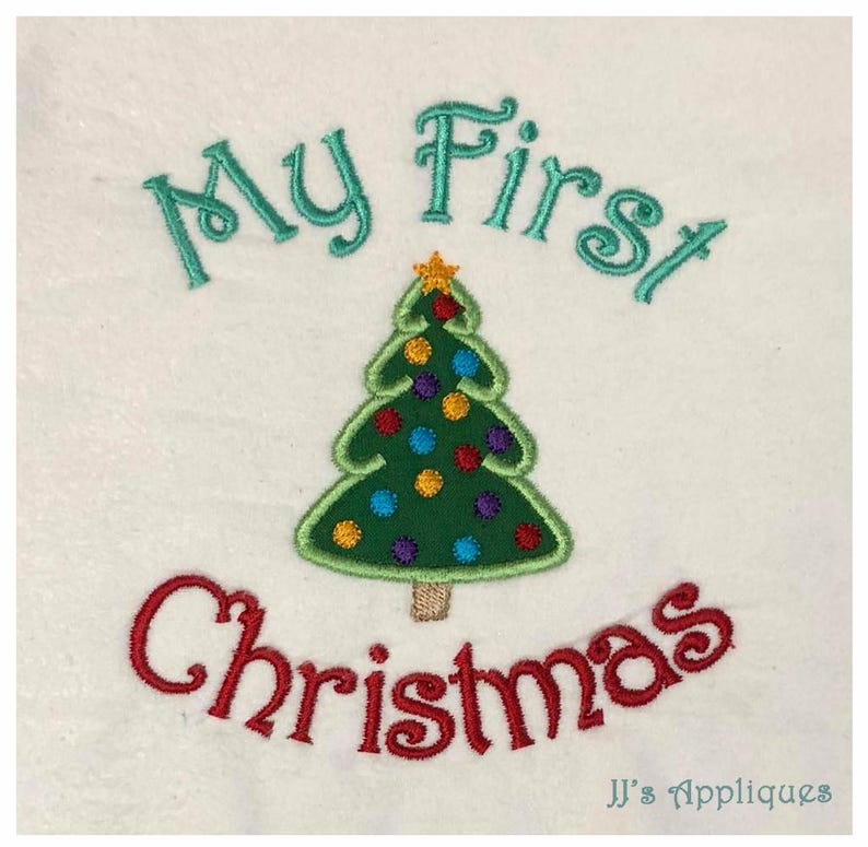 May include: An embroidered design on white fabric featuring a green Christmas tree with colorful ornaments and a yellow star topper. The text "My First" is stitched in teal above the tree, and "Christmas" is stitched in red below the tree.