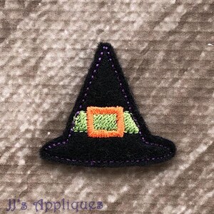May include: A black felt witch hat applique featuring purple stitching along the edges. The hat includes a light green band and a bright orange square buckle embroidered in the centre. The design is triangular with a wide, flat brim.
