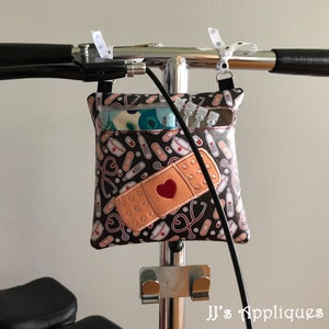 May include: A black and brown fabric bag with a red heart and a bandage design. The bag is attached to a silver walker with a black strap.