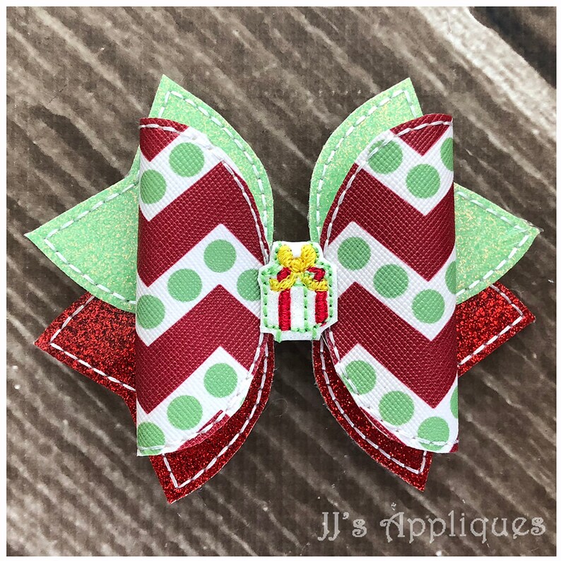 Op de afbeelding: Een rode en groene kerst strik met witte stippen en een chevron patroon. De strik heeft een klein groen en rood cadeaudoosje met een gele strik in het midden.