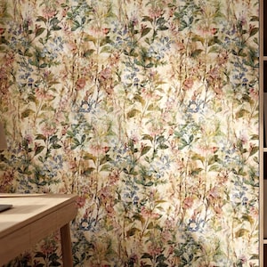 May include: Floral wallpaper with a vintage aesthetic. The design features a repeating pattern of flowers and foliage in shades of pink, blue, green, and cream. The wallpaper is installed on a wall in a room with a desk, lamp, and bookshelf.