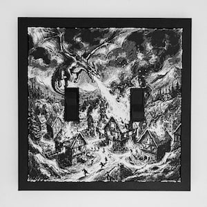 May include: A black and white double light switch cover featuring a detailed illustration of a dragon flying over a village and breathing fire onto a building. The scene includes small figures running through the streets amidst the flames and smoke.