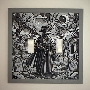 May include: A square double light switch wall plate featuring a black and white graphic illustration of a plague doctor standing in a graveyard with tombstones, bare trees, and a crescent moon in the sky, framed by a solid gray border.