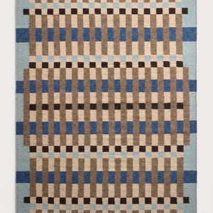 Puede incluir: Una alfombra rectangular con un patrón geométrico de bandas verticales y horizontales en tonos marrón, marrón oscuro, azul claro y azul medio. El diseño consiste en rayas que se cruzan creando una apariencia de cuadrícula.