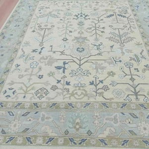 Close-up of the wool rugs surface, showcasing the sleek hand-knotted zero-pile texture and olive green chevron border.