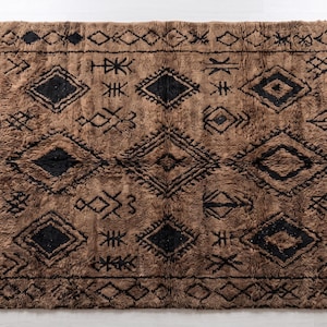 May include: A rectangular area rug featuring a deep brown, shaggy pile with a repeating pattern of black geometric diamond shapes and various linear symbols. The rug is framed by a thin black border and finished with short, light-colored fringe.