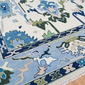 Overhead shot of an oushak rug ivory field with vibrant blue borders and scattered botanical motifs.