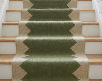 Könnte beinhalten: Ein Treppenläufer mit einem sich wiederholenden geometrischen Muster in Olivgrün und Naturbeige. Der Läufer ist über Holzstufen verlegt, wobei der strukturierte Stoff die Mitte jeder Stufe und Setzstufe in einem durchgehenden vertikalen Design bedeckt.