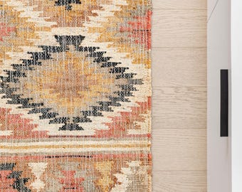 Könnte beinhalten: Ein rechteckiger Webteppich mit einem sich wiederholenden geometrischen Muster in den Farben Beige, Creme, Schwarz und Koralle. Die Textur wirkt grob und faserig, wobei die Webstruktur auf der gesamten Oberfläche des Bodenbelags sichtbar ist.