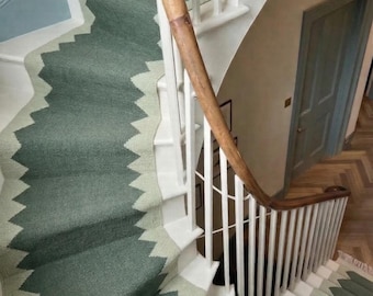 Könnte beinhalten: Eine Treppe mit einem Läufer in einem dunkelgrünen und hellgrünen Zickzackmuster. Die Treppe hat weiße Setzstufen und einen hölzernen Handlauf. Der Läufer bedeckt die Mitte der Stufen und erzeugt ein geometrisches Design entlang der Kurve.