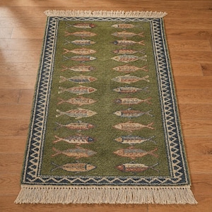May include: A rectangular area rug featuring an olive green background with two vertical columns of small, multi-colored fish motifs. The rug is framed by a dark blue border with a white zigzag pattern and finished with cream-colored fringe.