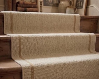 Könnte beinhalten: Ein gewebter Treppenläufer in hellem Beige mit strukturierter Oberfläche und zwei vertikalen, ockerfarbenen Streifen, die über die gesamte Länge verlaufen. Der Läufer ist auf Holzstufen verlegt und bedeckt Tritt- und Setzstufen.