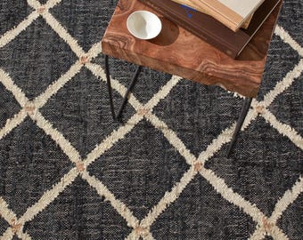 Könnte beinhalten: Ein schwarzer Teppich mit einem weißen Rautenmuster und kleinen beigen Akzenten an den Schnittpunkten. Der Teppich hat eine strukturierte, gewebte Optik und liegt unter einem hölzernen Beistelltisch mit Büchern und einer kleinen weißen Schale.