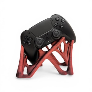 Könnte beinhalten: Ein schwarzer PlayStation 5-Controller liegt auf einem rot-braunen Holzständer. Der Ständer hat ein einzigartiges, organisches Design mit mehreren verzweigten Stützen. Der Controller verfügt über verschiedene Tasten und Richtungstasten.