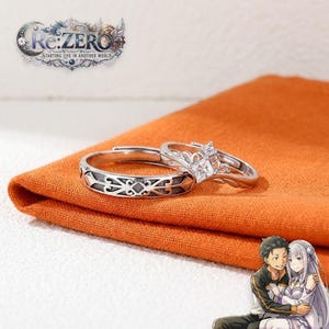 Puede incluir: Dos anillos plateados con el logotipo de Re:ZERO Starting Life in Another World. Uno tiene un patrón grabado intrincado, mientras que el otro presenta un engaste en forma de corona con una piedra cuadrada transparente. Incluye una ilustración anime.