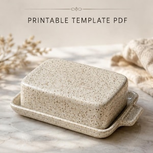 Könnte beinhalten: Eine rechteckige Butterdose aus Keramik mit gesprenkelter beiger Oberfläche, bestehend aus einem passenden Deckel und einem Unterteil mit kleinen seitlichen Griffen. Der Text CERAMIC BUTTER DISH PRINTABLE TEMPLATE PDF und INSTANT DOWNLOAD sind sichtbar.