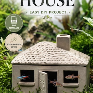 Puede incluir: Una casa de acuario de cerámica con el texto "CERAMIC AQUARIUM HOUSE" y "EASY DIY PROJECT". La casa beige tiene una chimenea, un tejado de tejas y ventanas con peces en su interior. También se muestra una plantilla PDF y una guía paso a paso.