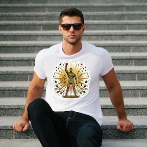 May include: A white t-shirt featuring a central graphic of a standing figure with one arm raised in a fist. The figure is filled with a colorful geometric pattern in red, green, yellow, and black, surrounded by gold sunburst rays and stars.