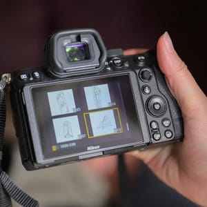 Puede incluir: Una cámara digital Nikon negra que muestra imágenes en su pantalla. La cámara se sostiene en una mano, con la pantalla mostrando varias miniaturas de fotos. La correa de la cámara es visible y la pantalla muestra el logotipo de Nikon.