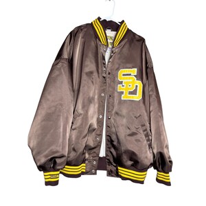 May include: Brown satin jacket with yellow and white accents. Features a yellow and white "SD" logo on the front. The jacket has a button-up closure, ribbed cuffs, and a collar with yellow stripes. A classic sports-themed jacket.