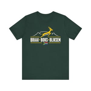 May include: A dark green short-sleeve t-shirt featuring a graphic print of a yellow leaping antelope silhouette above a white mountain outline. The text reads BRAAI BOKS BLIKSEM in white capital letters, accompanied by a small South African flag.