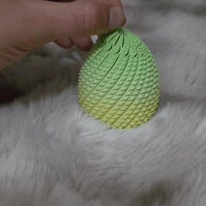 May include: A 3D-printed, egg-shaped object with a textured surface. The top is a vibrant green, gradually fading into a yellow hue at the bottom. The object is held by a hand.