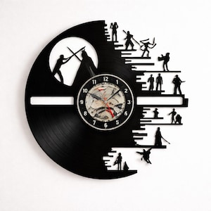 Könnte beinhalten: Schwarze Vinyl-Schallplattenuhr mit Star Wars-Motiv. Die Uhr hat ein zentrales Zifferblatt mit sichtbaren Zahnrädern und Zeigern. Silhouetten von Figuren sind um das Zifferblatt herum ausgeschnitten, mit einer Kampfszene und einem Mond.