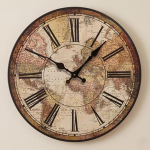 Peut inclure: Une horloge murale ronde avec un fond représentant une carte du monde de style ancien dans des tons beige, rose et marron. Le cadran affiche des chiffres romains noirs et deux aiguilles en métal noir. Une bordure sombre encadre le design.