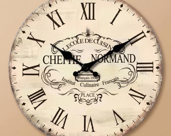 Könnte beinhalten: Eine runde Wanduhr mit cremefarbenem Zifferblatt, schwarzen römischen Ziffern und schwarzen Metallzeigern. In der Mitte steht der Text L'ECOLE DE CUISINE, CHEFIE NORMAND, Institut Culinaire Français und das Jahr 1930 in dekorativer Schrift.