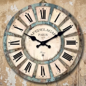 May include: A round wall clock with a distressed, vintage design. The clock face features Roman numerals, black hands, and the text "CAFEDELAGAR PARIS 1870". The clock has a light blue and white color scheme, with a weathered appearance.