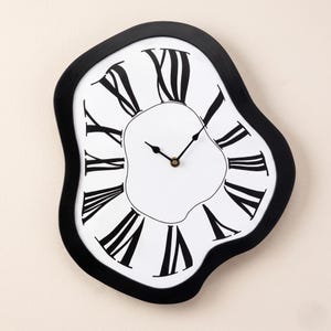 May include: A wall clock with an irregular, melting-style black frame and a white face. The clock features black Roman numerals arranged in a distorted, wavy pattern around the center, with two black hands indicating the time on the dial.