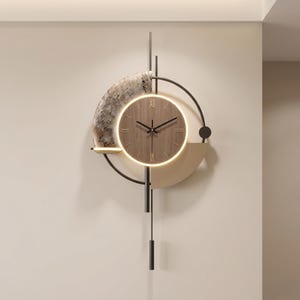 Puede incluir: Un reloj de pared con esfera circular de grano de madera y números romanos, iluminado por un anillo LED cálido. El diseño incluye un semicírculo con patrón de mármol, un semicírculo beige sólido, detalles en metal negro y un péndulo.