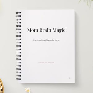 May include: A white spiral-bound notebook titled "Mom Brain Magic" with the subtitle "The Mental Load Planner for Moms." The cover also includes the phrase "Release your perfection." A pencil and a bowl of popcorn are in the background.