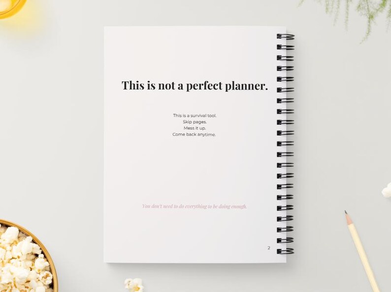 May include: A white spiral-bound planner with the text "This is not a perfect planner." Additional text includes "This is a survival tool. Skip pages. Mess it up. Come back anytime."