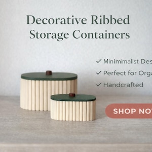 May include: Two decorative ribbed storage containers with green lids and a minimalist design. The containers are handcrafted and have a light beige ribbed exterior. The image includes the text "Decorative Ribbed Storage Containers" and "Shop Now".