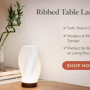 May include: A white, ribbed table lamp with a warm glow, featuring a modern and minimalist design. The lamp has a wooden base and is next to a glass vase with green plants. The text "Ribbed Table Lamp" is at the top.