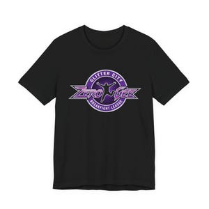 Puede incluir: Camiseta negra con un diseño morado y blanco. El diseño incluye las palabras "Glitter City Breakfight League" y "Zero Gee" con la silueta de una persona. Camiseta de cuello redondo y manga corta.