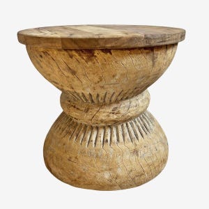 May include: A handcrafted wooden stool with a unique hourglass shape. The stool features a round top and base, connected by a carved, textured midsection. The natural wood grain and color variations are visible throughout the piece.
