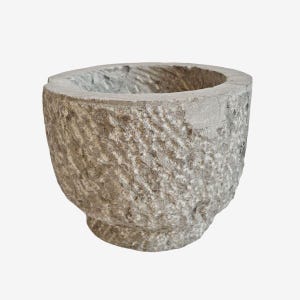 May include: A weathered, gray stone mortar with a rough, textured exterior. The mortar has a wide, open bowl shape and a small, rounded base. The interior shows signs of use, with visible wear and tear.