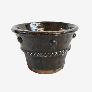 May include: A dark brown ceramic planter with a textured surface. The planter has a rope-like design around the middle and three raised circular accents. The rim is slightly flared.
