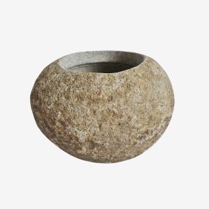 May include: A round, stone-like bowl with a wide opening. The bowl has a rough, textured surface with shades of tan, brown, and gray. The interior is a darker gray. This decorative bowl could be used for plants or as a unique home accent.