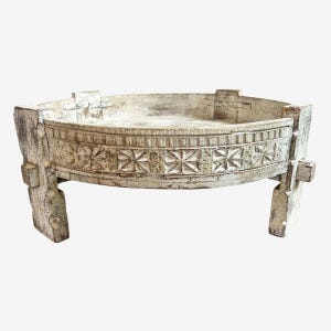 May include: A distressed, off-white wooden tray table with carved geometric patterns. The tray has a low profile and is supported by four sturdy legs. The tray's rim features a repeating starburst design. The table is likely for decorative use.