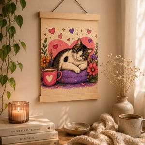 Könnte beinhalten: Gerahmter Kunstdruck mit einer Katze, die auf einem lila Kissen in Herzform liegt, umgeben von Blumen und Herzen. Eine rosa Tasse mit Herz ist ebenfalls zu sehen. Der Druck wird in einem hellen Holzrahmen präsentiert.