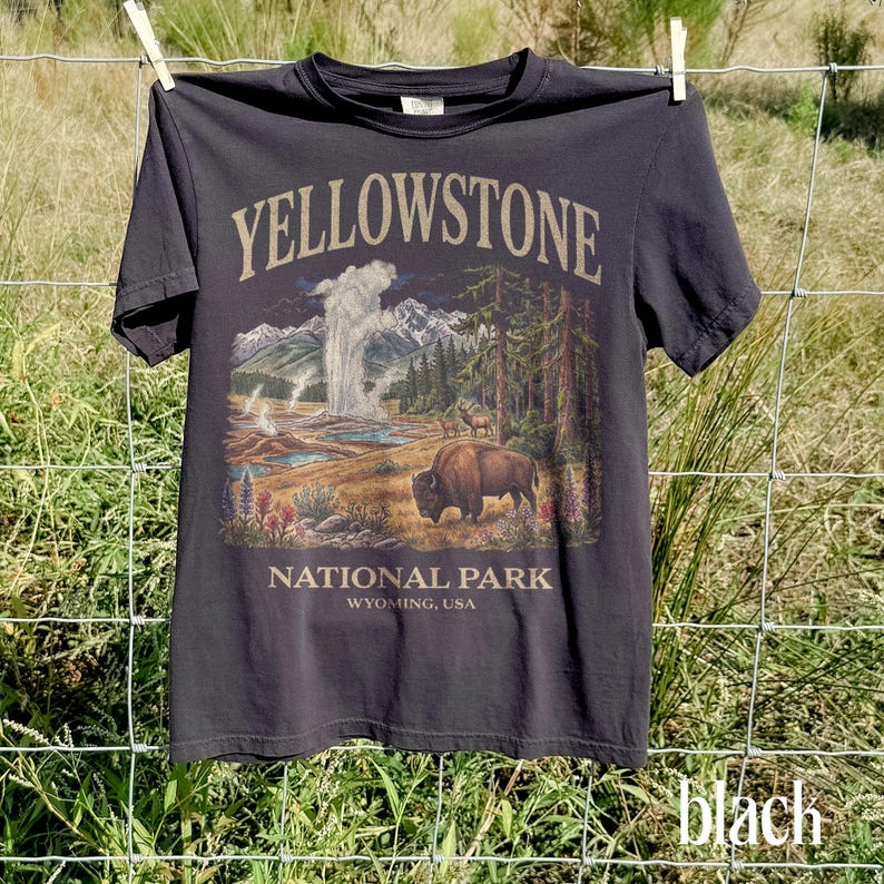 May include: Black t-shirt featuring a Yellowstone National Park design. The graphic includes a bison, geyser, mountains, and trees. The text "YELLOWSTONE NATIONAL PARK WYOMING, USA" is printed on the shirt.