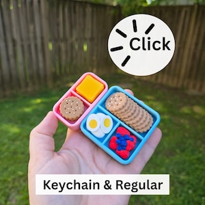 May include: Miniature food-themed keychain and regular-sized items. The pink and blue containers hold tiny replicas of crackers, cheese, eggs, and berries. The image includes the text "Click" and "Keychain & Regular".