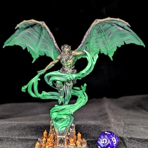 May include: A detailed miniature figure of a winged creature with green wings and a flowing green energy effect. The figure stands on a detailed base with small figures and a purple, multi-sided die.